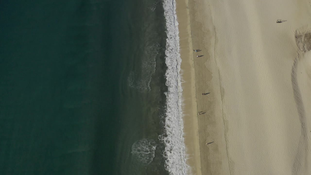 Vertical drone view of surf beside empty sand