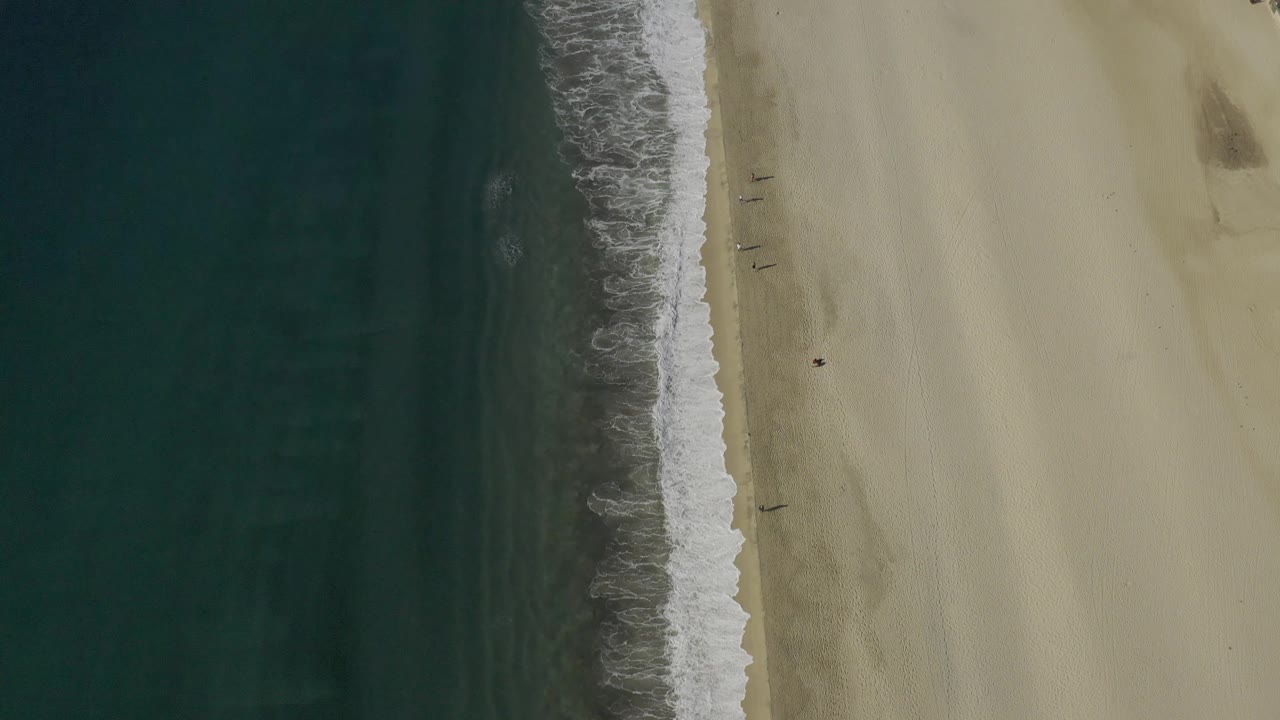 Drone view over Baja California Sur with the surf line slightly farther right, dark water filling the left side, broad pale beach on the right, and no visible people.