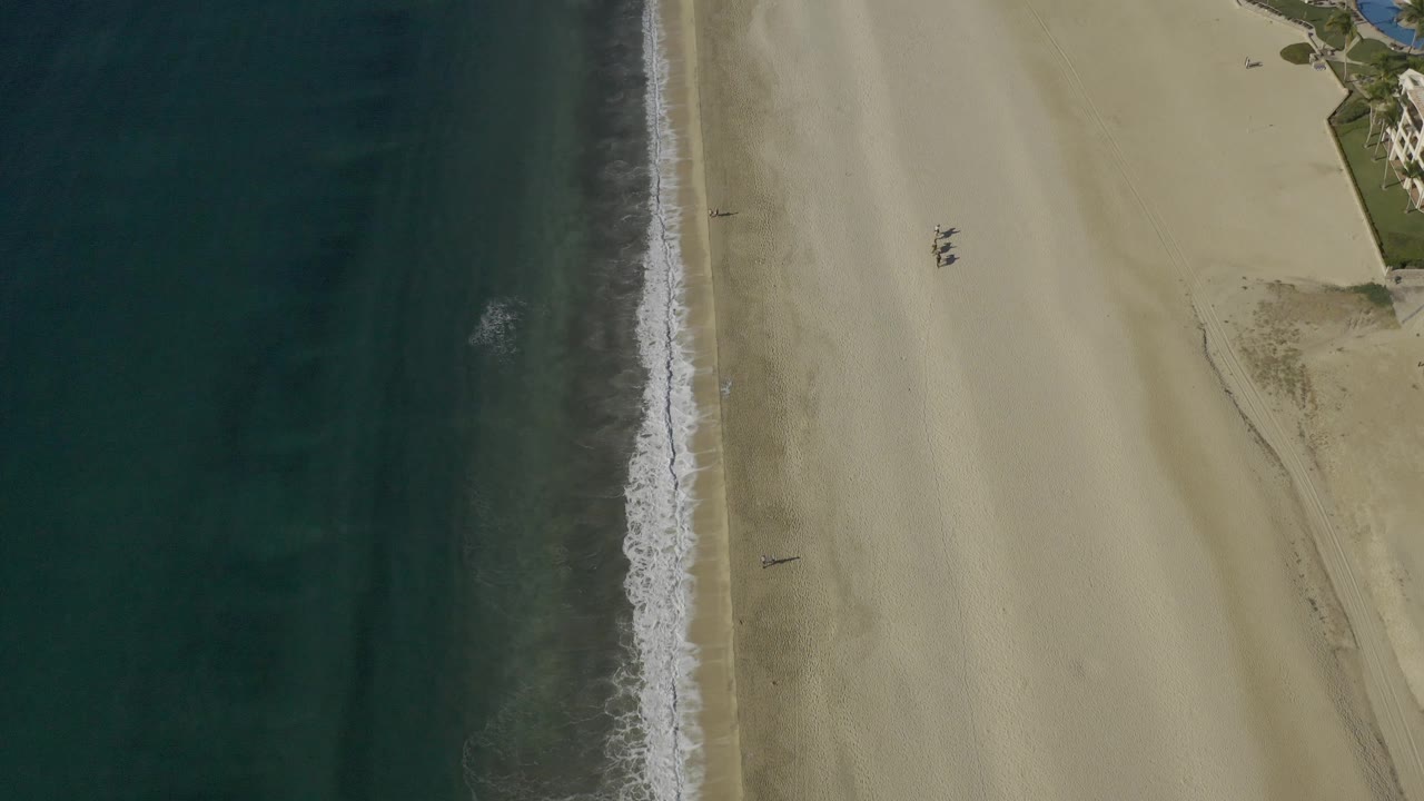 Vertical bands of ocean, foamy surf, and pale beach from above.