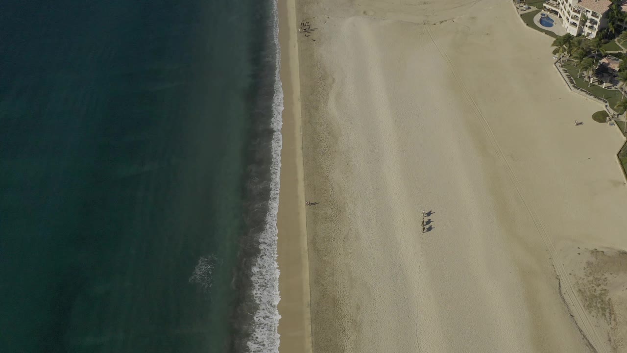 Aerial beach view with surf line and apartment buildings near the sand.