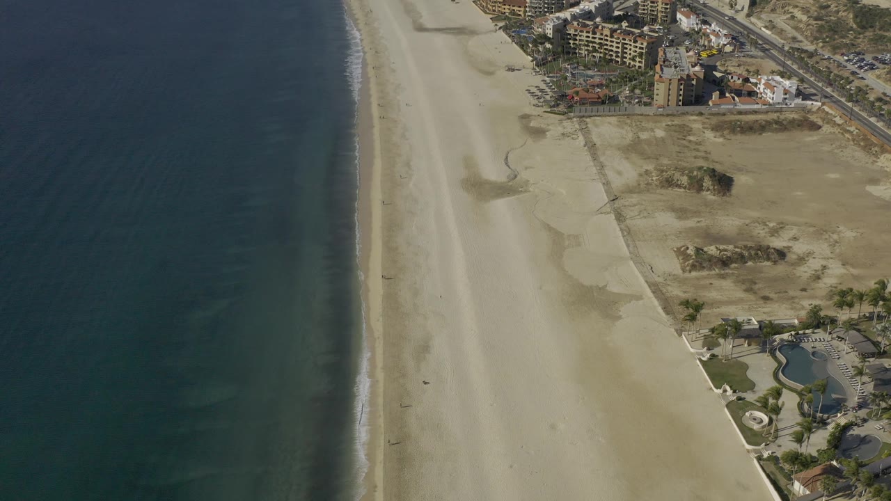 Aerial view of blue water beside a long empty beach and dry inland land.