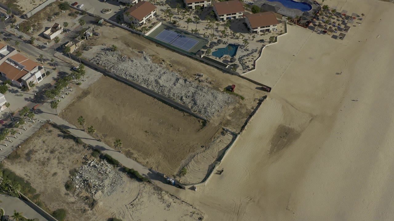 Aerial view of walled sandy parcels and nearby houses with pools.