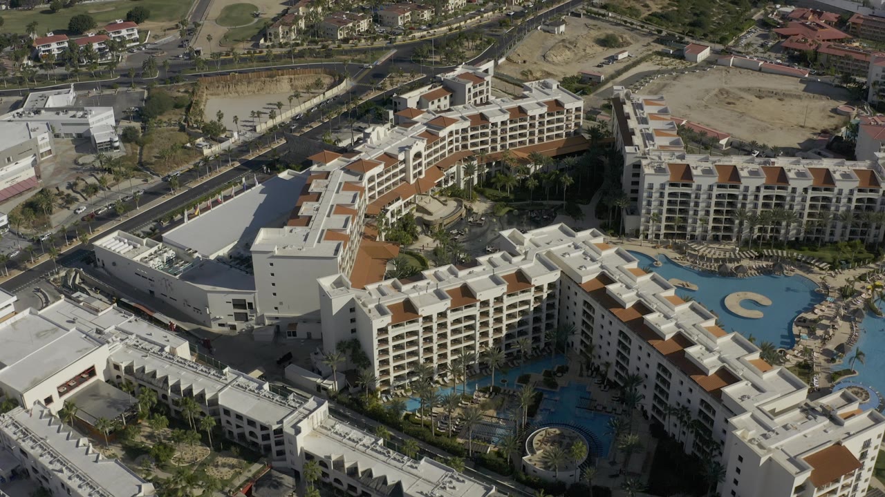 Aerial resort complex with curved blue pool and white buildings.