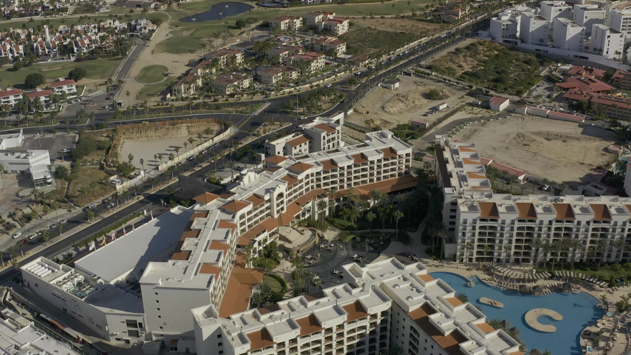 Third frame shows a wide Baja California Sur drone view with hotel-style blocks, a pool in the lower right, roads, golf greens, dry lots, residential areas, and no visible people.
