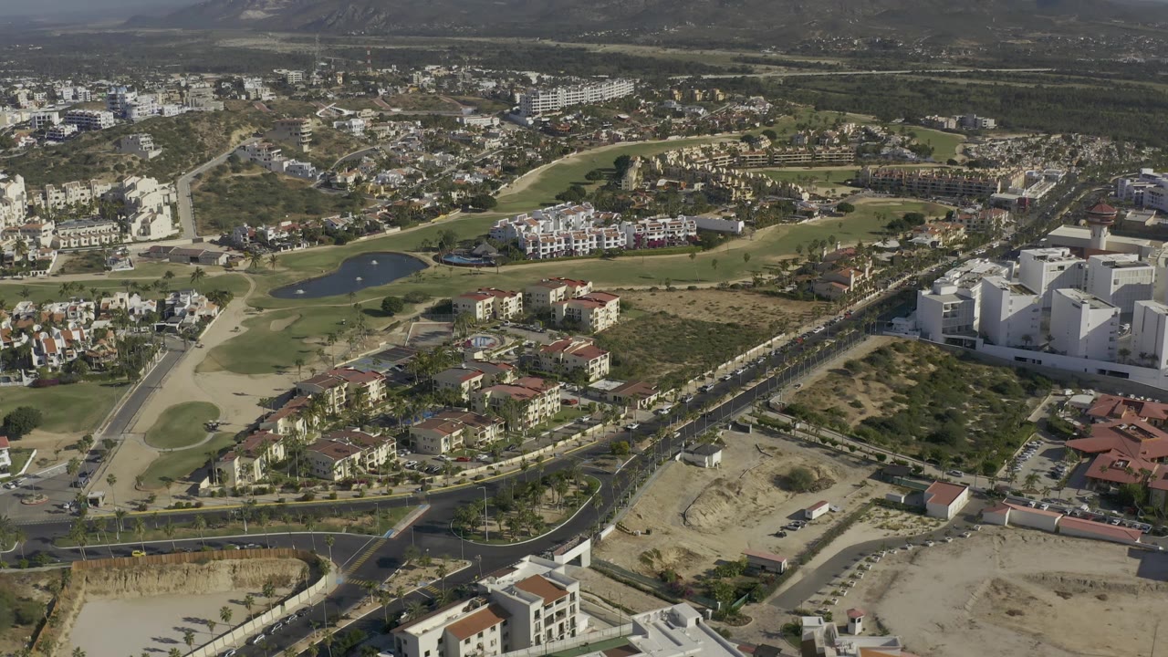 Aerial town view with a curved road, clustered homes, ponds, and large white buildings.