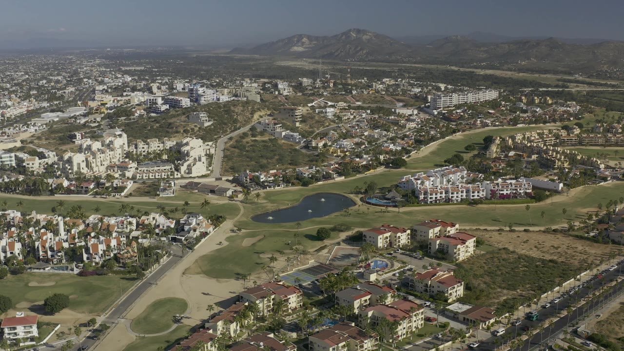 Aerial city view with lake, fairways, residential buildings, dry lots, roads, and mountains in the distance.