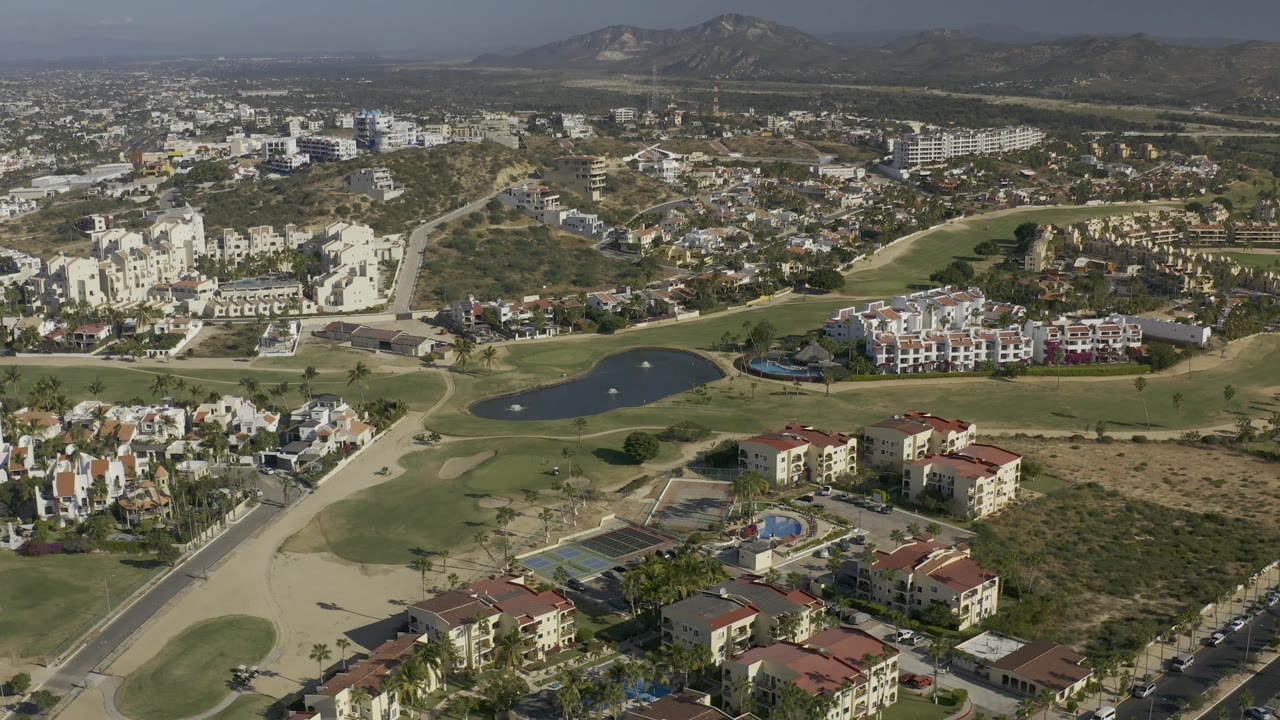 Aerial neighborhood view with pond, fairways, buildings, roads, and dry land.