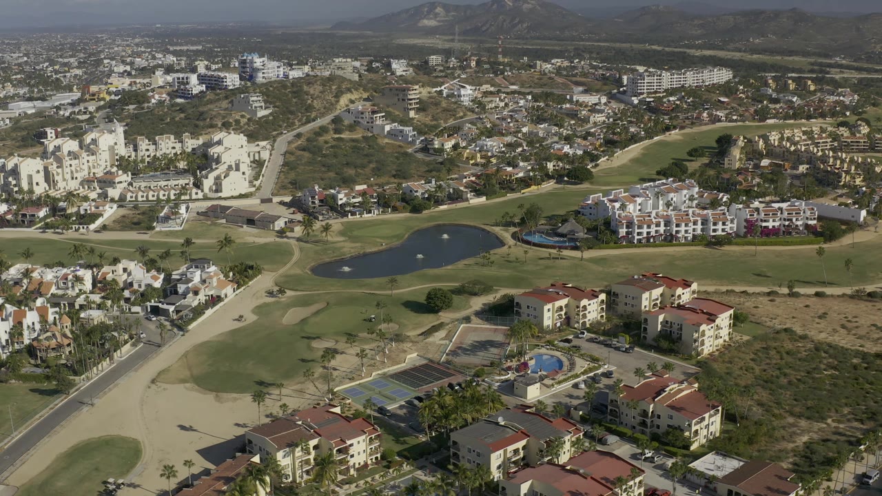 Drone view across condos, tennis courts, golf greens, and a small lake.