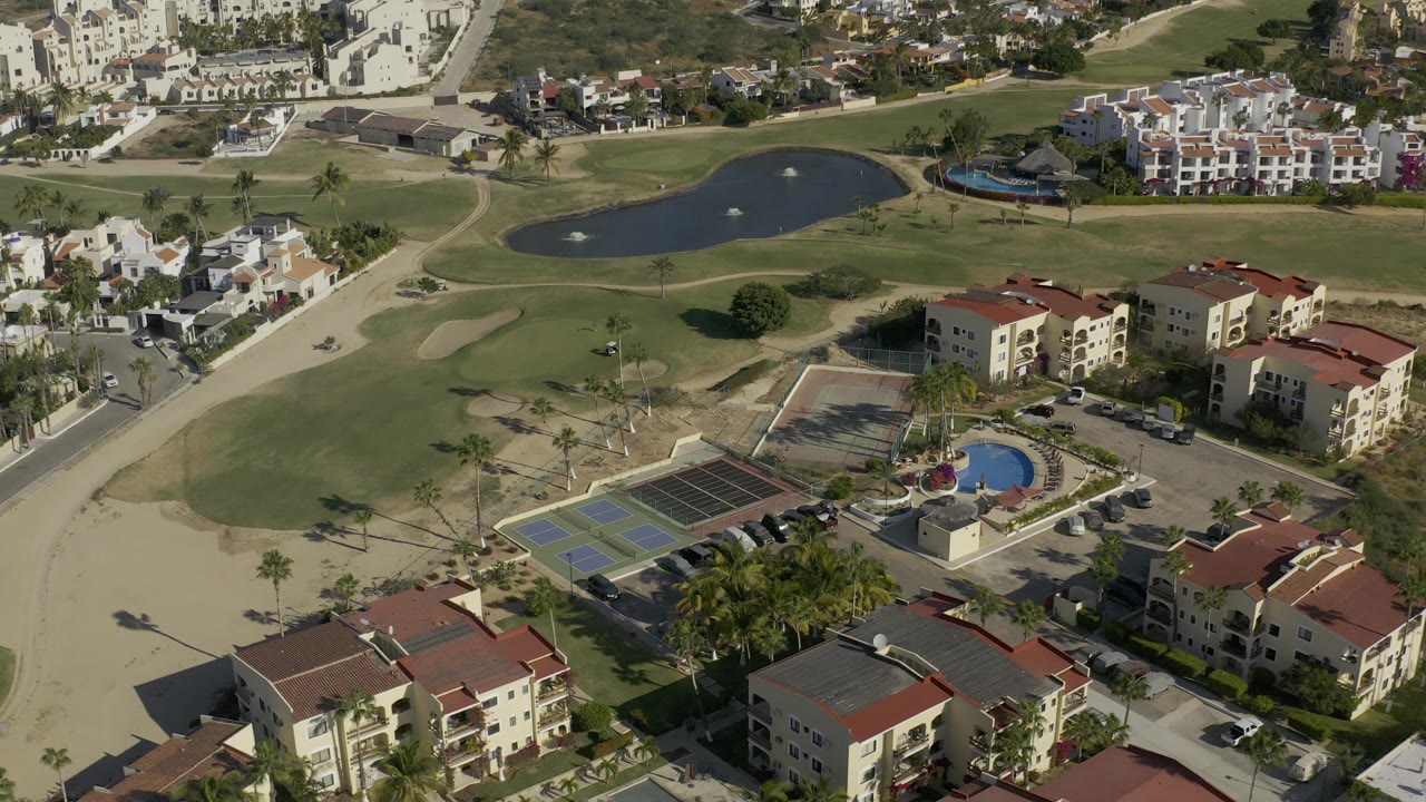 Aerial view with apartment roofs in front, tennis courts, pool, fairways, and ponds beyond.