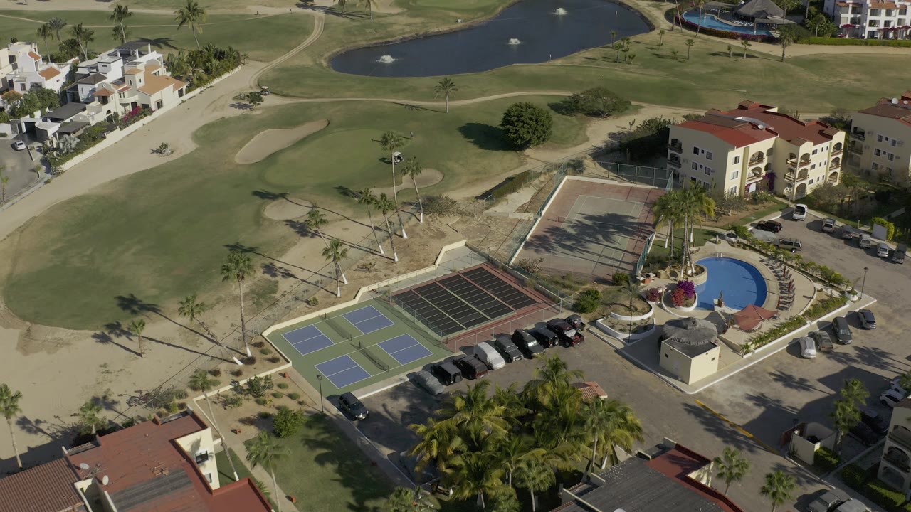 Aerial angle over golf green, sand trap, road, tennis courts, pool, and adjacent buildings.