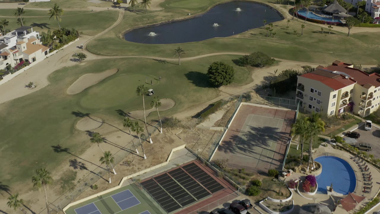 Drone view over fairways, residential buildings, courts, and a pond.