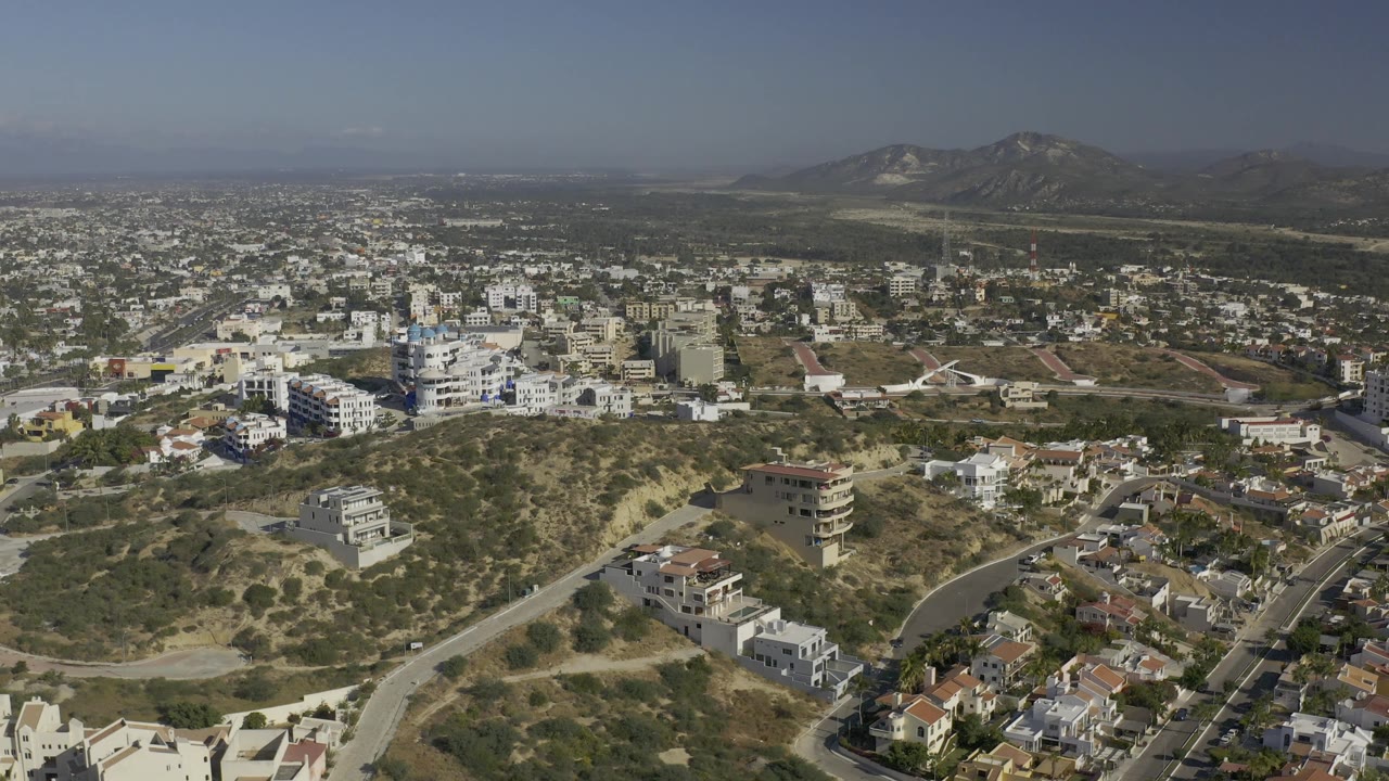 Aerial view across residential blocks and open dry hills with mountains beyond.