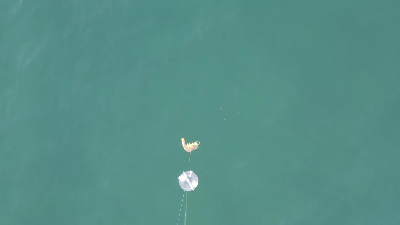Top-down view over Baja California Sur water with a small pale object above a bright circular float and faint tether lines, with no visible people.