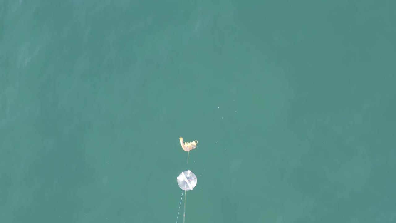 Small object and round float over calm blue-green water.