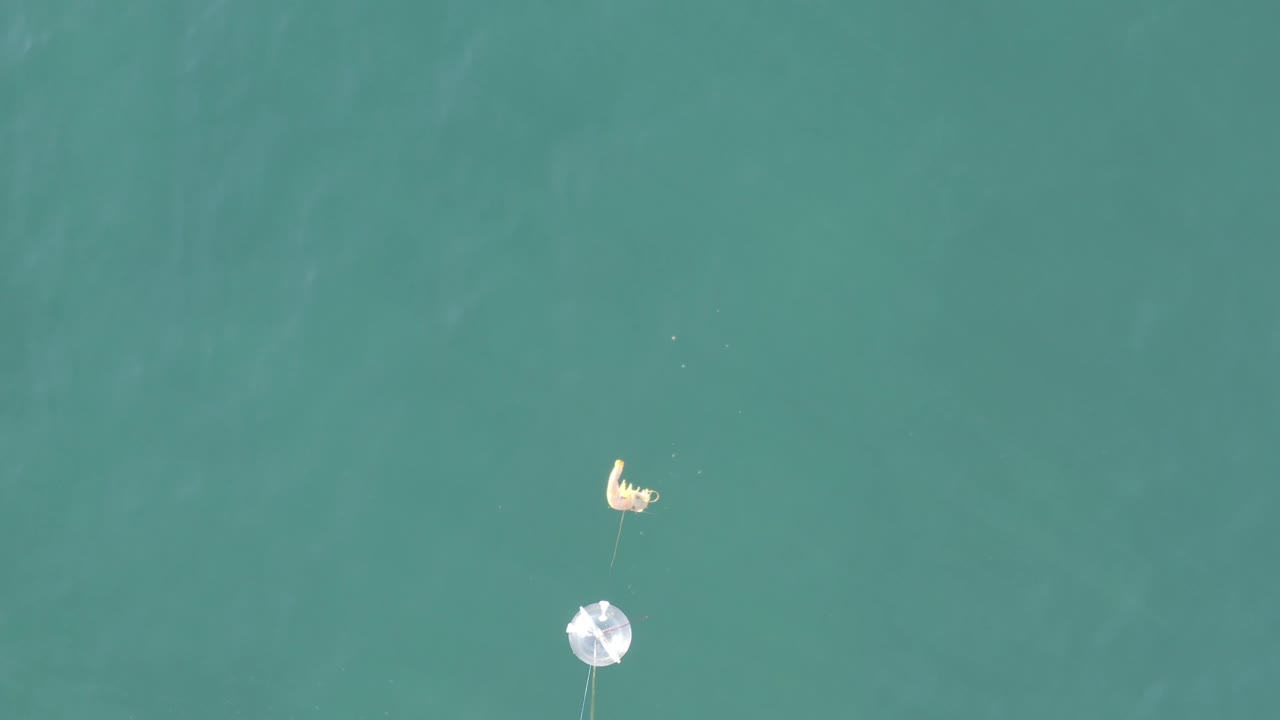 Top-down Baja California Sur view where the yellow float sits above the white circular float, with thin lines extending downward through lightly textured turquoise water.