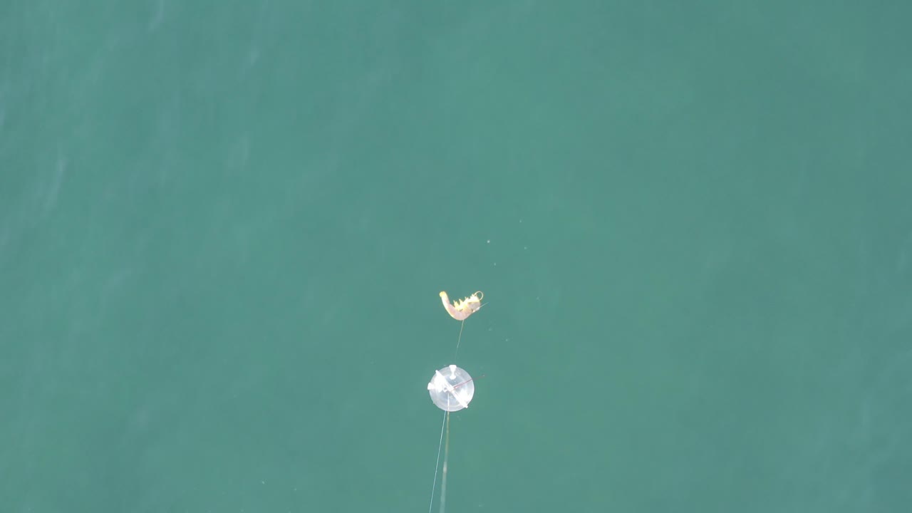 Overhead view of turquoise sea in Baja California Sur, Mexico, with a small pale floating object above a reflective round piece and no visible people.