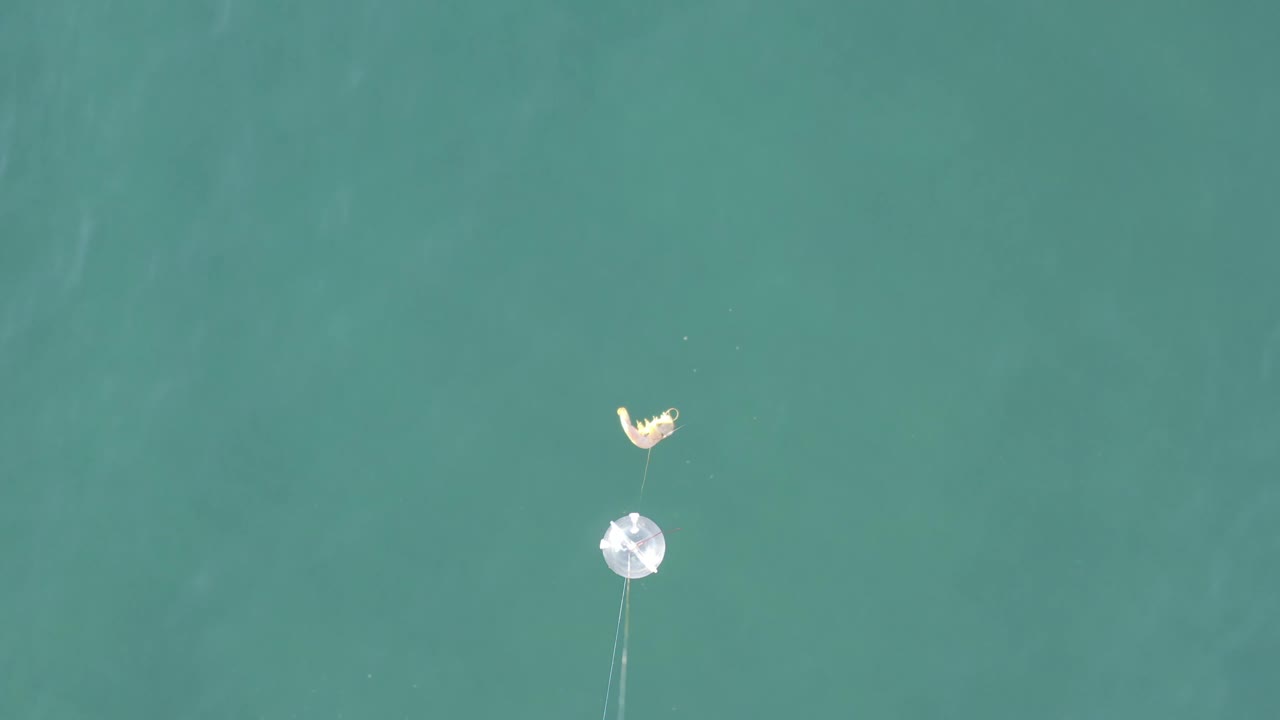 A small debris cluster sits high in the frame over green-blue water in Baja California Sur, Mexico, with the reflective round item separated below it and no visible people.