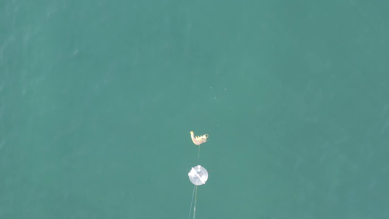Aerial ocean frame with a small pale marker and faint underwater lines.