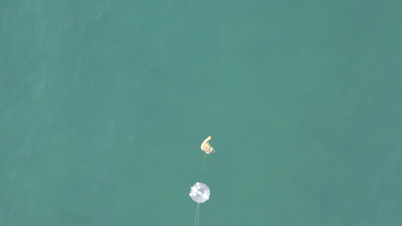 Overhead frame from Baja California Sur, Mexico showing a white fishing float or lure and pale curved tackle over turquoise water, with no visible people.