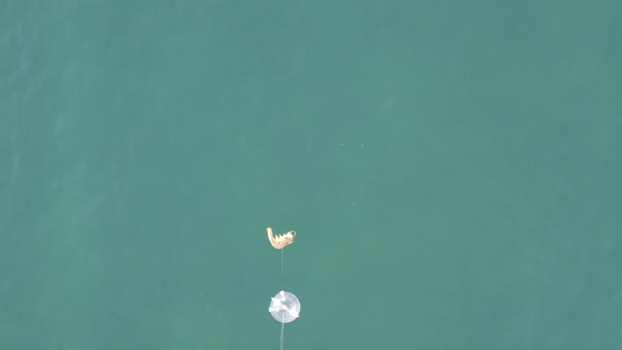 Overhead Baja California Sur water detail with the white float or lure and pale curved tackle separated by a short length of line, with faint water texture and no visible people.