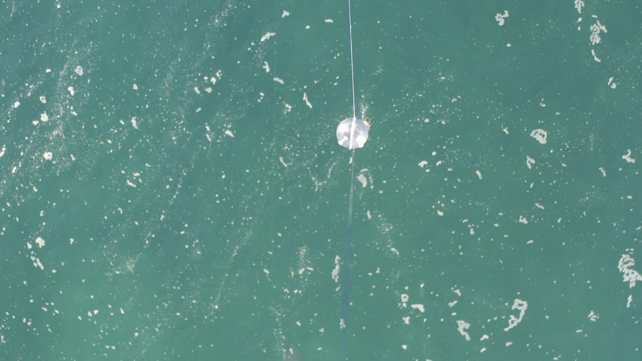Teal water with foam flecks and a white cotton ball hanging on thread near the upper frame.