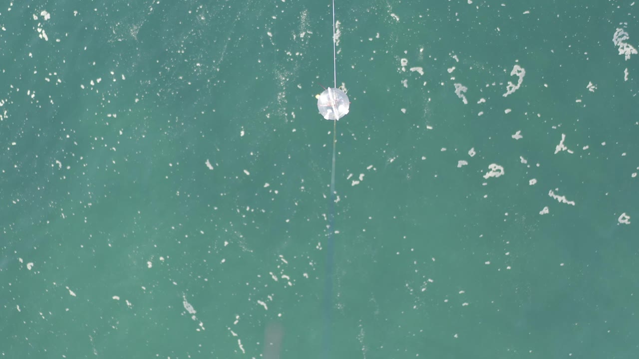 A Baja California Sur, Mexico water detail with teal surface texture, scattered white foam, and the cotton ball hanging on thread near the left third, with no visible people.