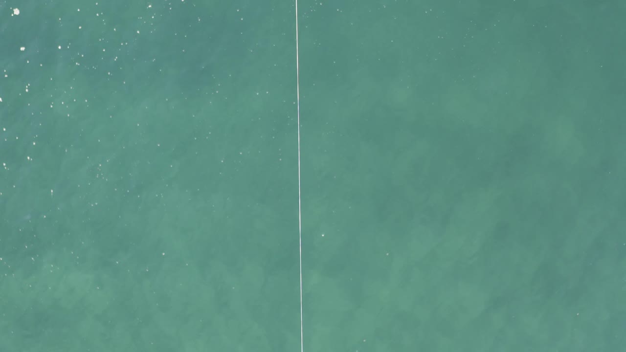 Turquoise water with a vertical line and white floating object near the top