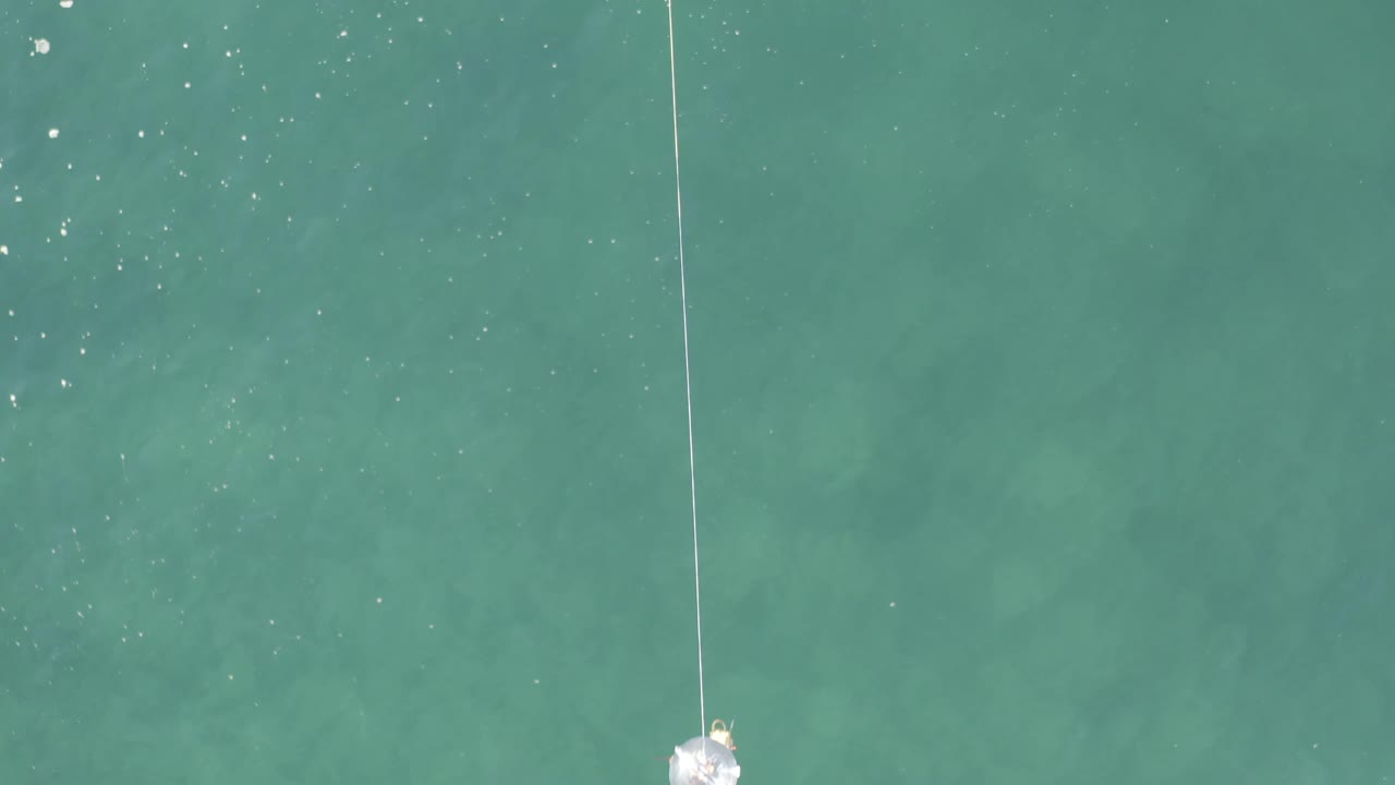 A thin line and bright lure sit against the clear green water of Baja California Sur Mexico, with small surface highlights and no visible people.