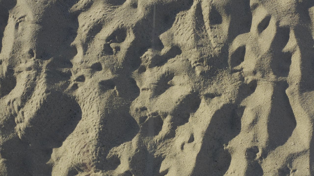 Sunlit sand in Baja California Sur fills the frame with overlapping footprints and raised ridges, while darker shadows define the pressed shapes and no visible people appear.