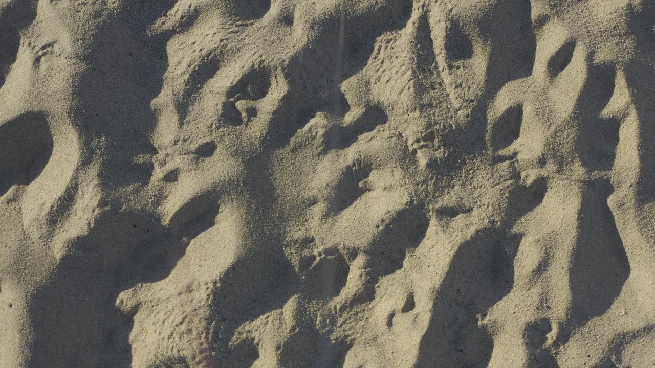 A tight view of Baja California Sur beach sand shows uneven mounds, narrow shaded pockets, and no visible people near the middle of the clip.