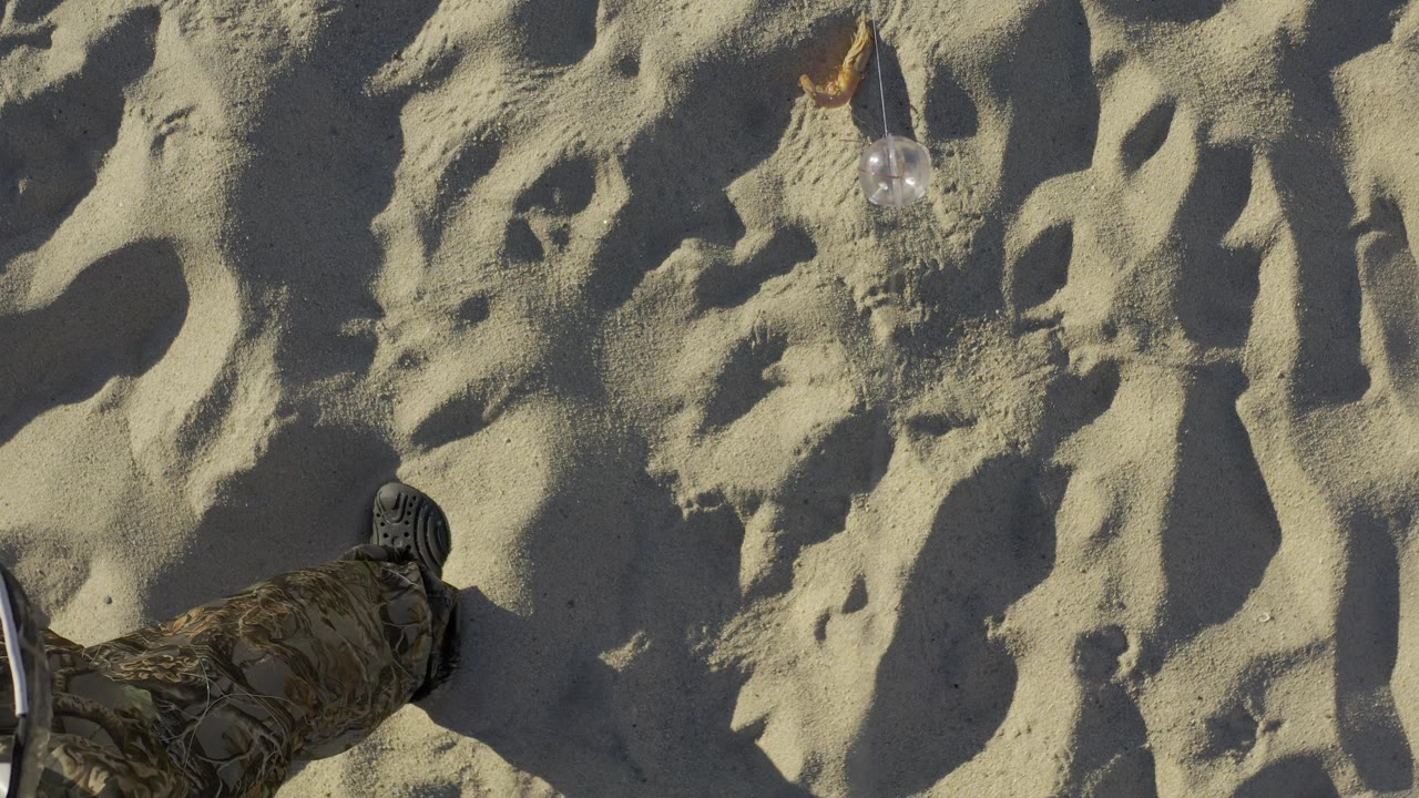 Rippled beach sand with a partial boot at the lower left and a small object near the top.