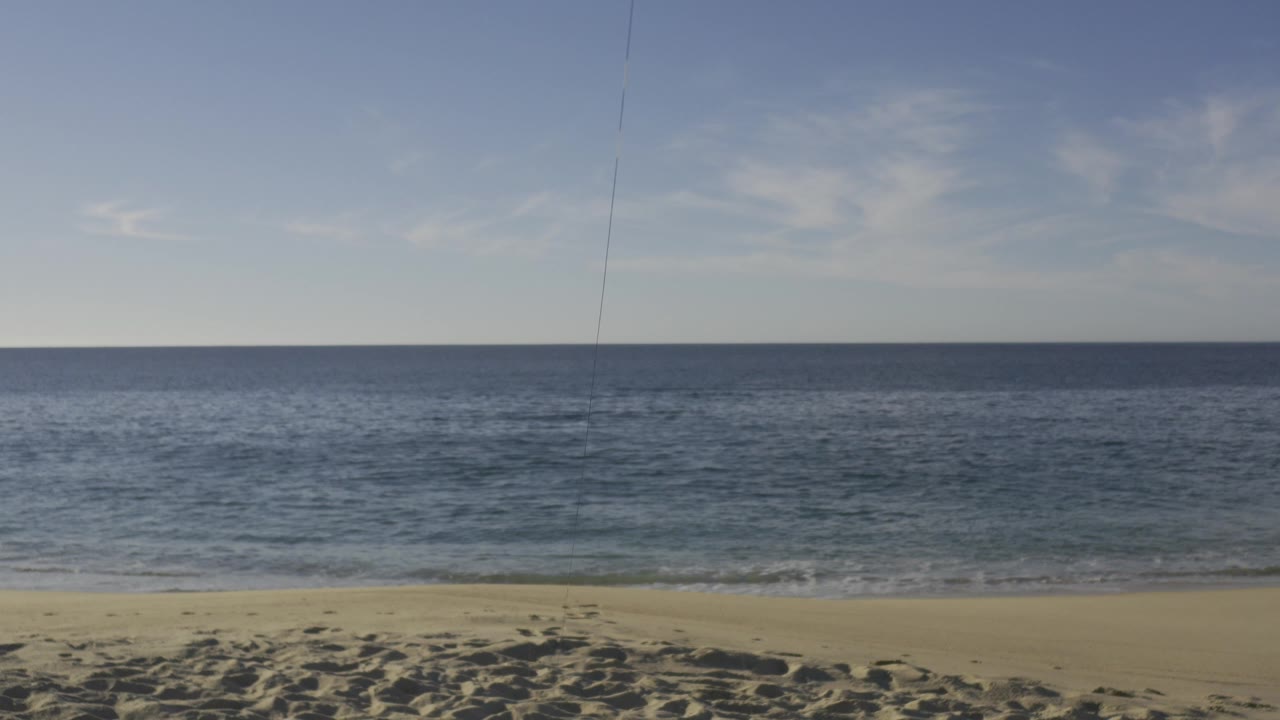 Wide view of a sandy Baja California Sur beach with blue ocean, a level horizon, pale sky, thin clouds, and no visible people at 0:00.