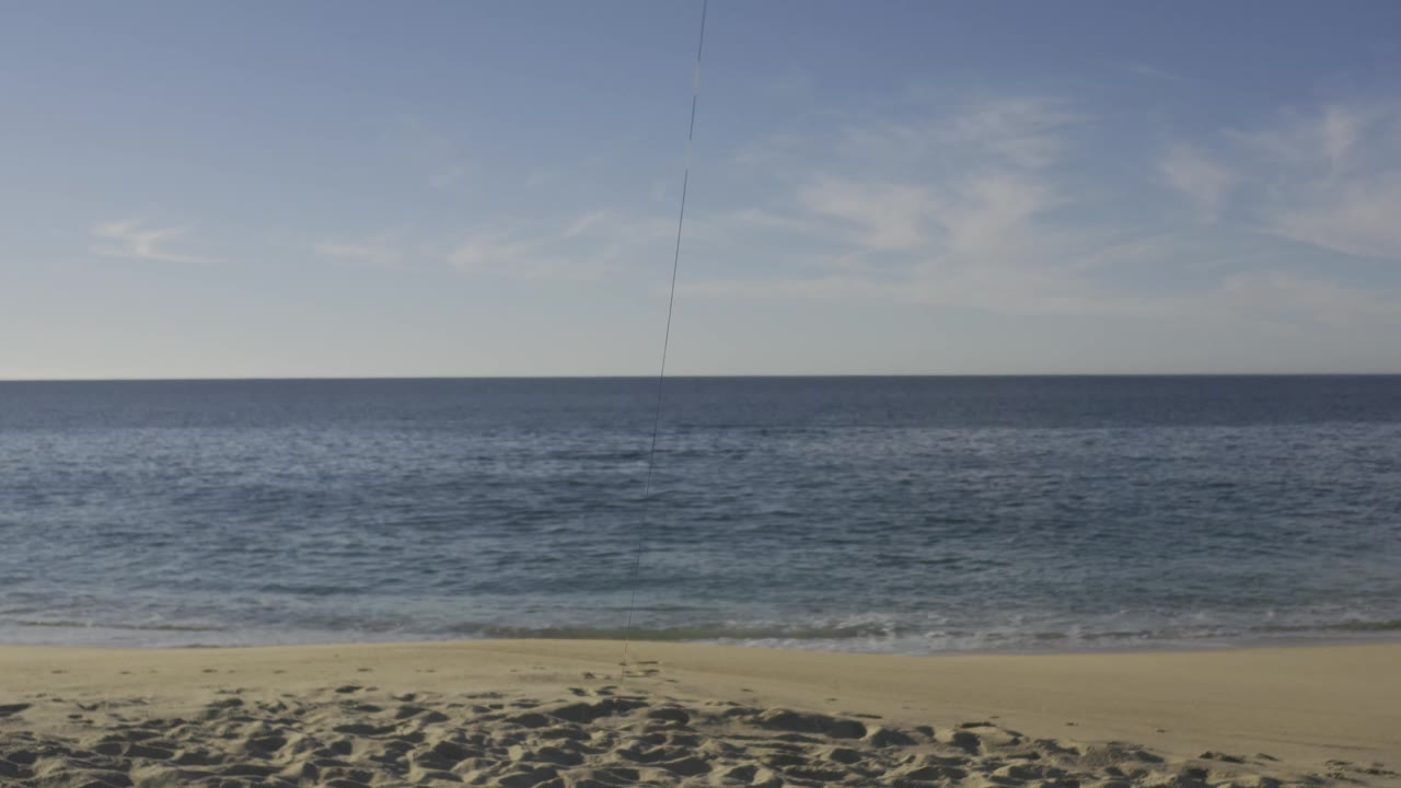 Wide Baja California Sur shoreline frame with a narrow wave line near the sand, darker blue water beyond, thin cloud cover, and no visible people at 0:01.