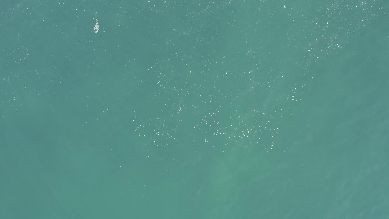 Overhead view of turquoise ocean in Baja California Sur, Mexico, with sparse white foam dots spread across the upper half and no visible people.