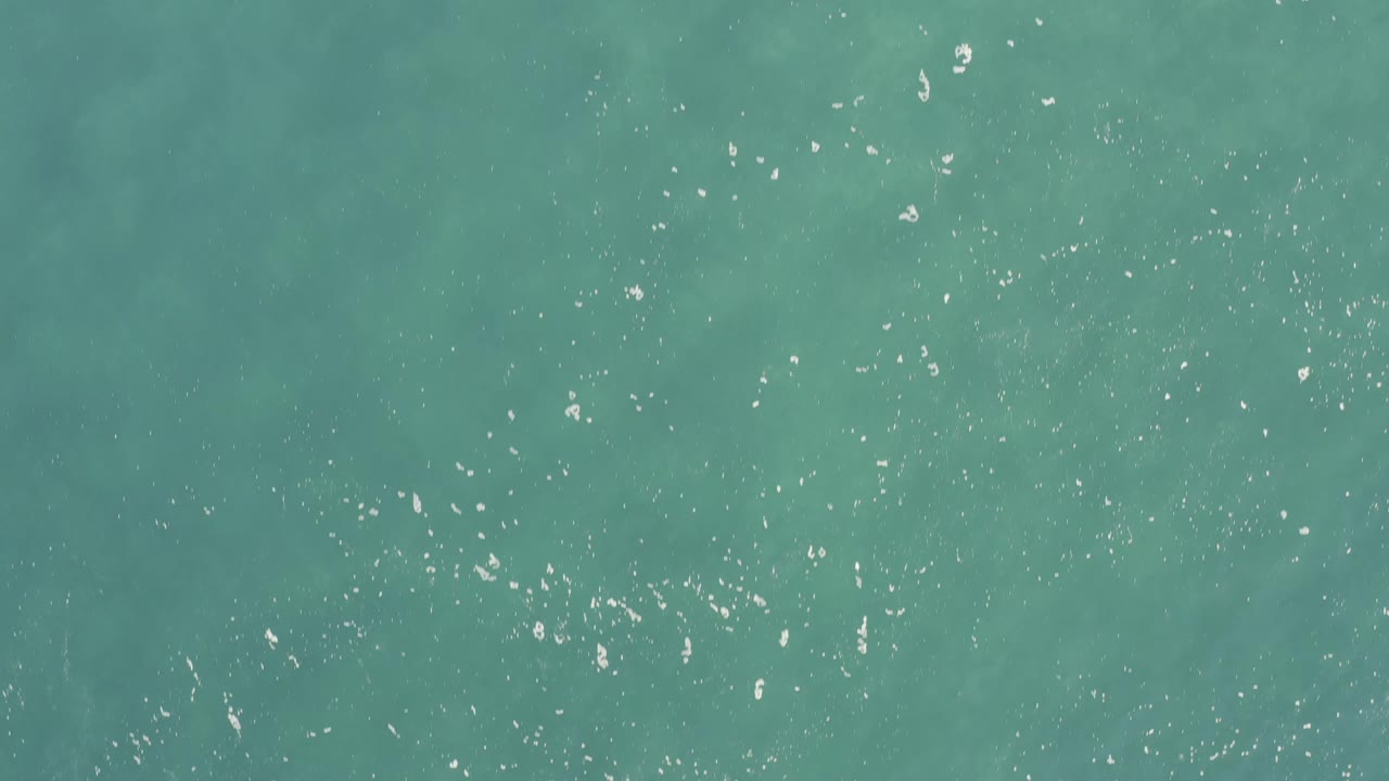 Aerial view of turquoise sea in Baja California Sur, Mexico, with brighter scattered highlights across the upper water and no visible people.