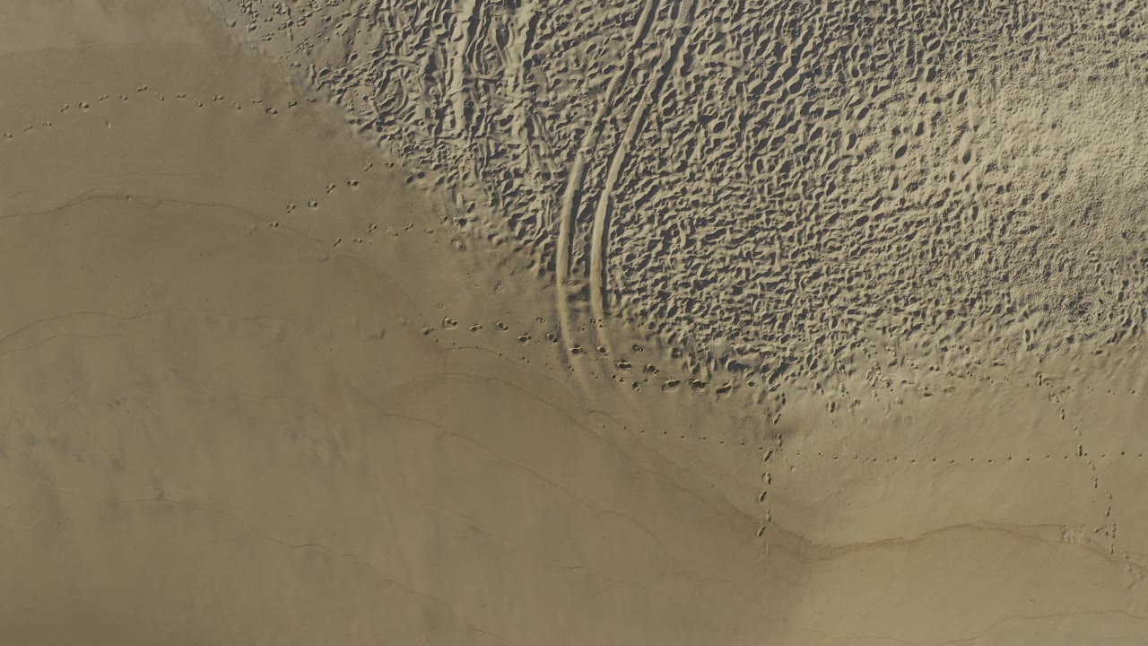 Top-down view of Baja California Sur sand showing dense ripples in the upper area, faint track lines through the center, and open smoother sand below, with no visible people.
