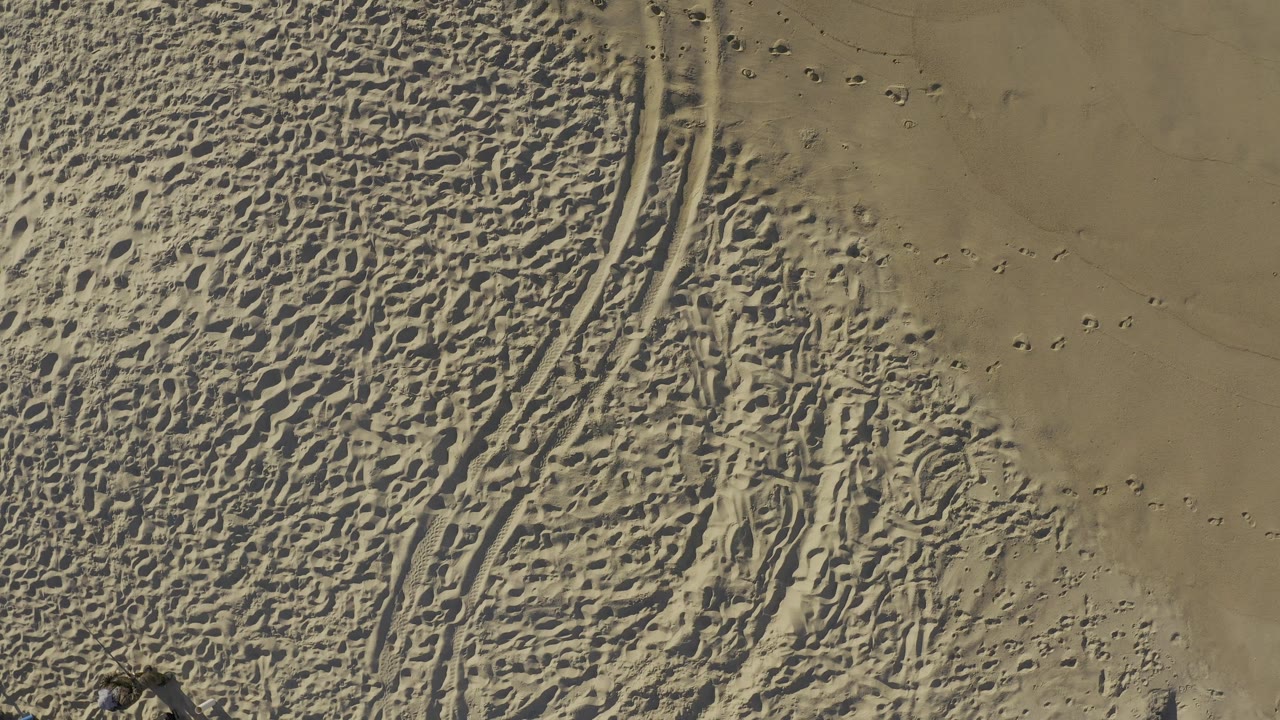 A later overhead frame from Baja California Sur, Mexico, with dense rippled texture on the left, smoother tan ground on the right, small dotted impressions, and no visible people.