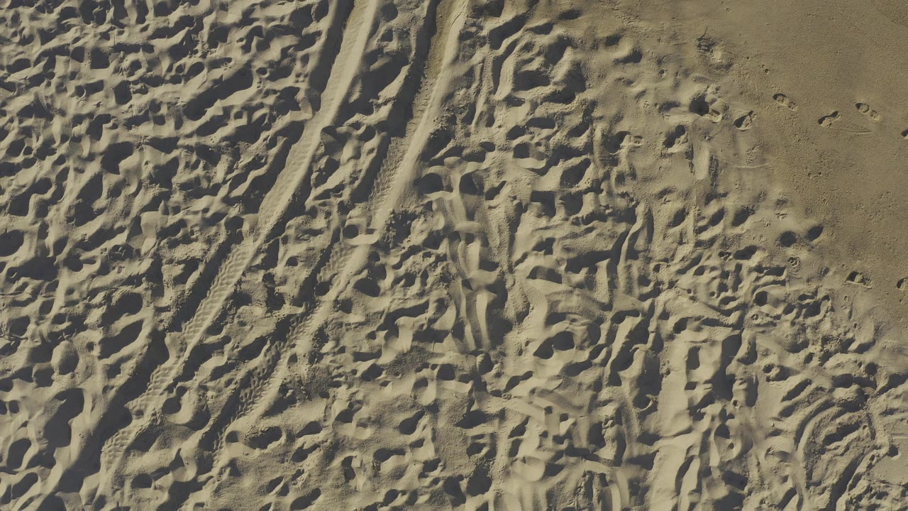 High overhead view of tan beach sand in Baja California Sur, Mexico, with dense footprints, track marks, and no visible people.