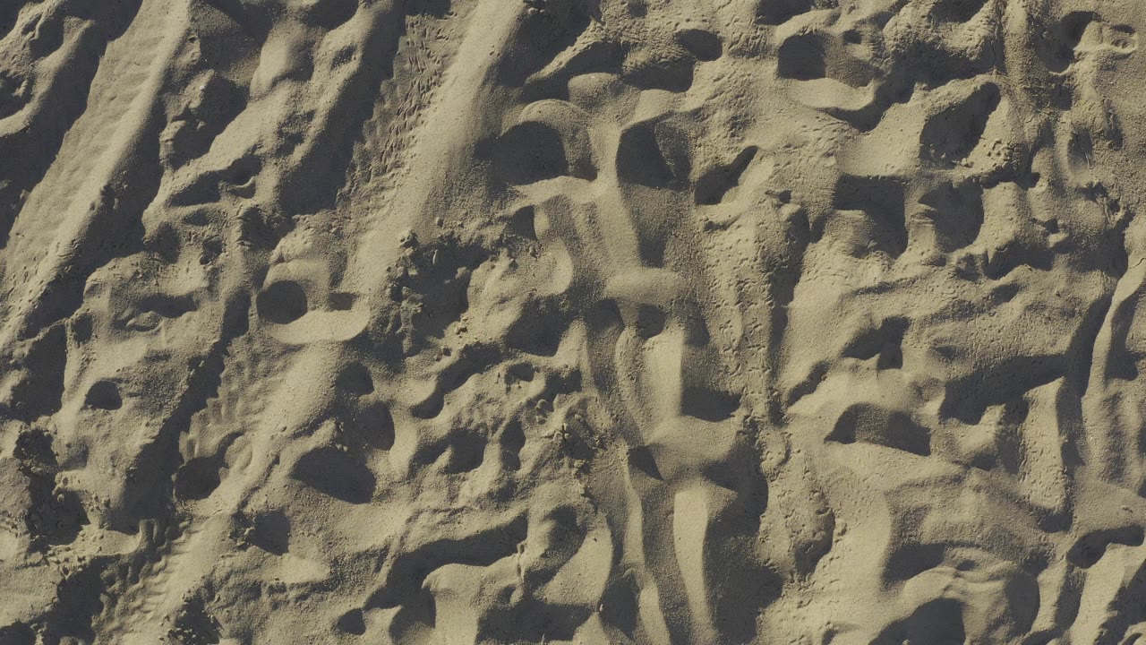 Overhead close view of sunlit sand texture in Baja California Sur, Mexico, with raised ridges, dark hollow impressions, and no visible people.