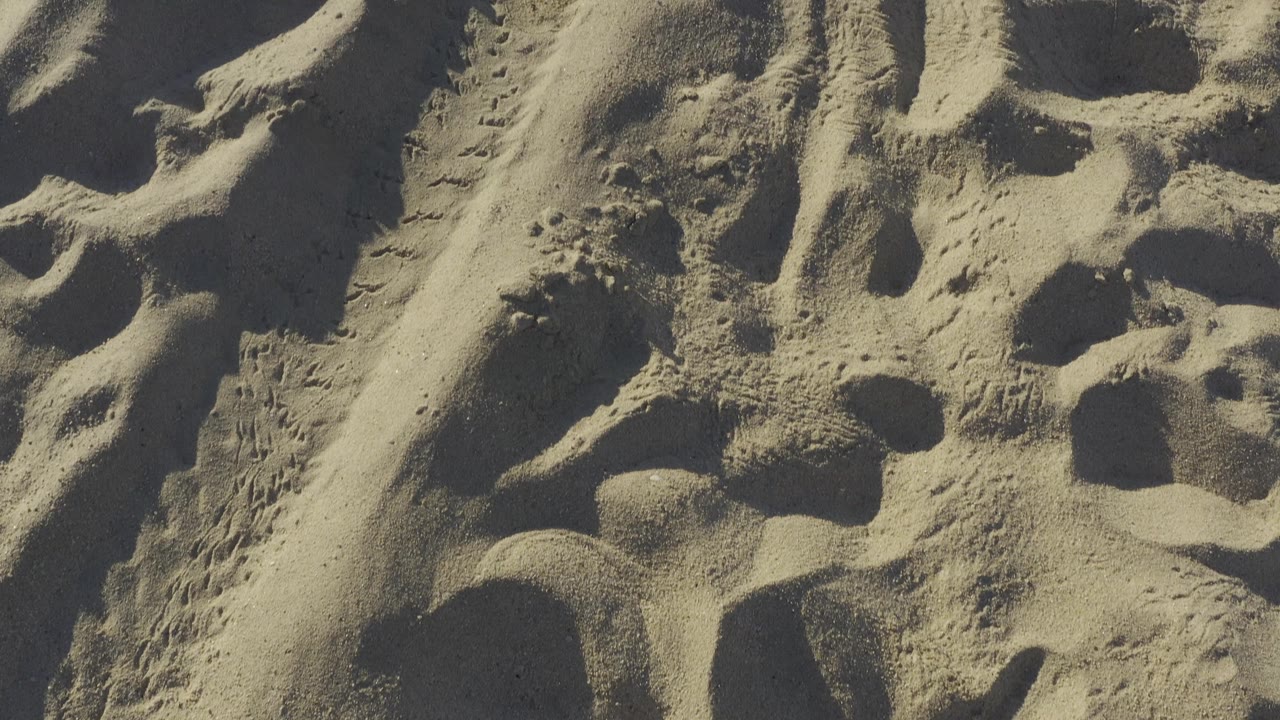 Close sand pattern in Baja California Sur, Mexico, showing footprint depressions, wind-smoothed patches, and angled shadows, no visible people.