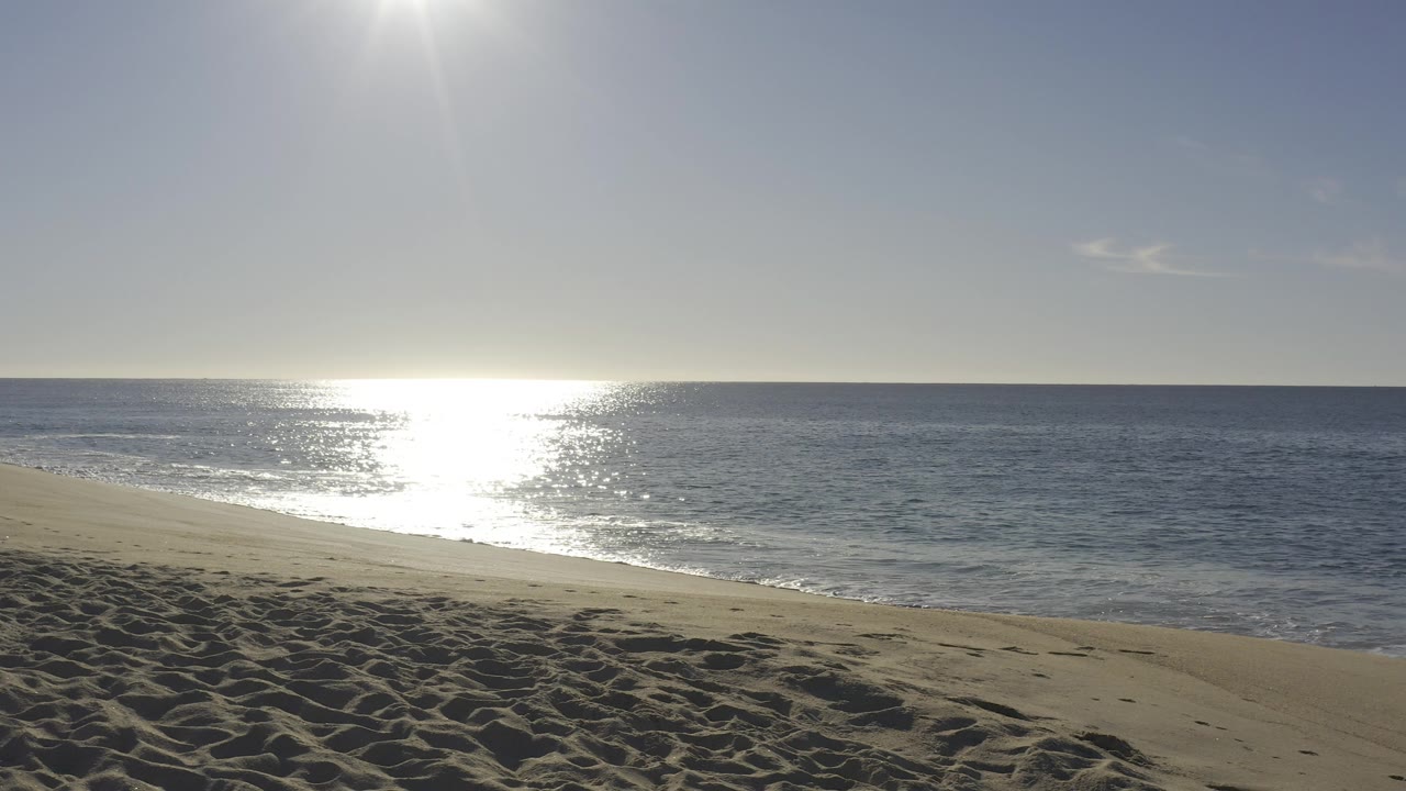 Baja California Sur beach view with bright sun glare on the ocean, a sandy foreground, and no visible people.