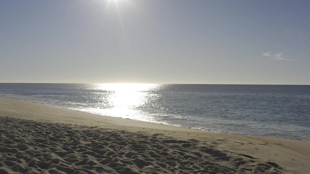 Baja California Sur shoreline with the sun reflecting across the water, beach sand in front, and no visible people.