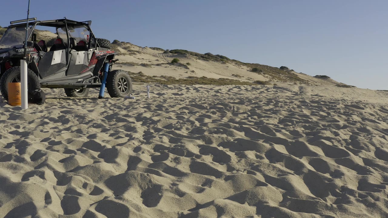 Parked off-road vehicle on Baja California Sur sand with low dunes behind it, a clear sky above, and no visible people.