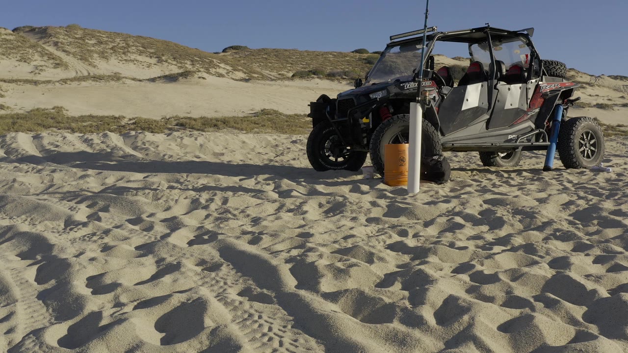 Parked off-road vehicle beside a pole on rippled beach sand.