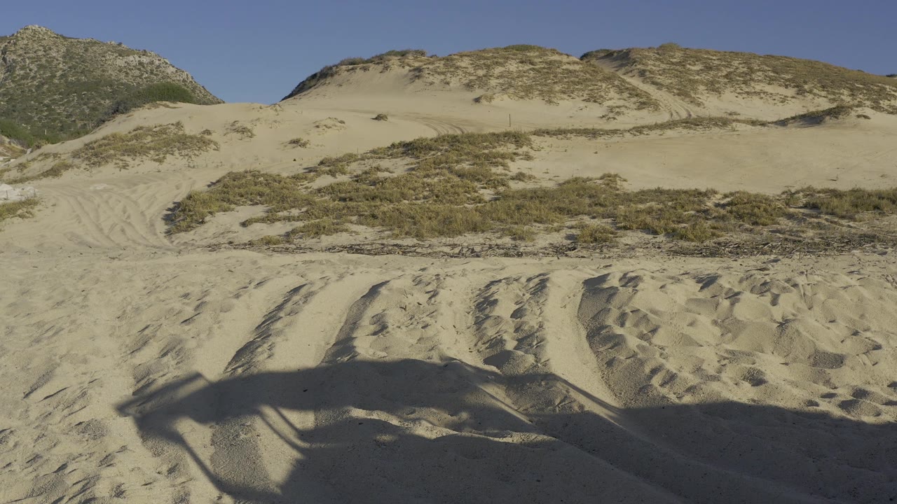 Baja California Sur desert dunes with a broad sandy foreground, brush-covered midground, sunlit ridge, and no visible people.