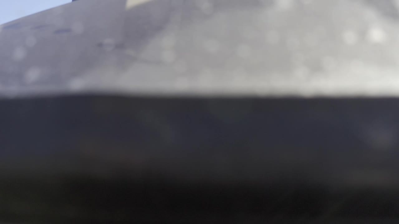 Blurred one-second frame from Baja California Sur showing a pale beach band across the top and darker coastal water below, with no visible people.
