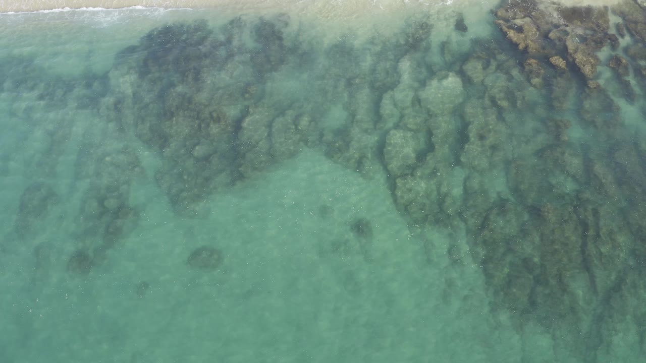 Overhead shallow blue-green water covering dark tan shoreline rocks.