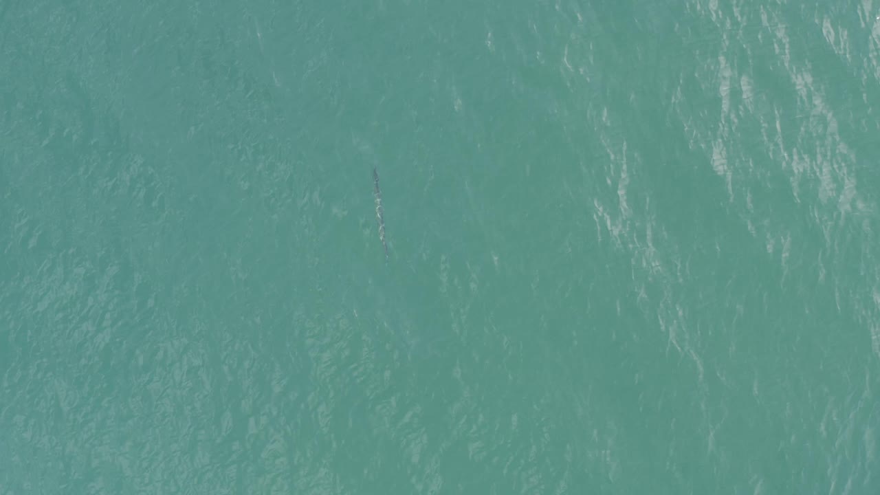 Aerial view of teal water in Baja California Sur, Mexico, with faint diagonal ripples, darker patches below the surface, and no visible people.
