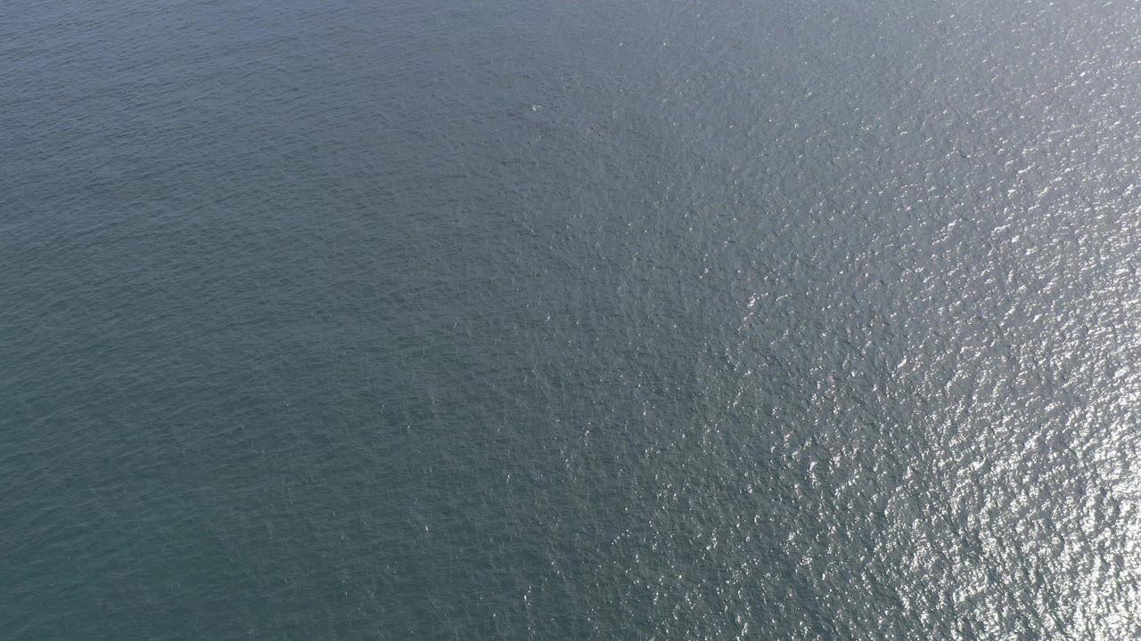 Overhead view of blue-green ocean surface in Baja California Sur, Mexico, with fine wind ripples and bright sun reflection on the right, no visible people.