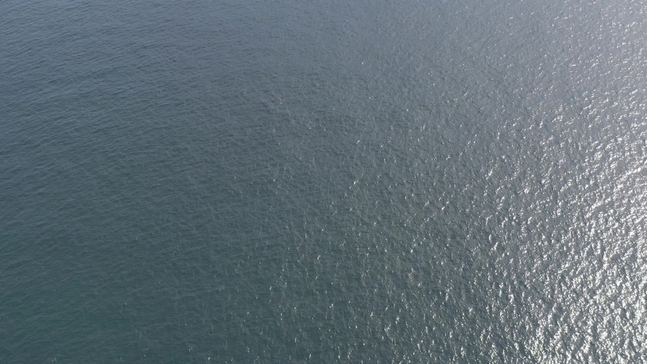 Aerial view of blue-green ocean in Baja California Sur with a broad silver sun reflection across rippled water and no visible people.
